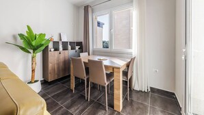 Un espace de vie compact comprenant un coin repas, un canapé, une plante et une fenêtre avec des rideaux.