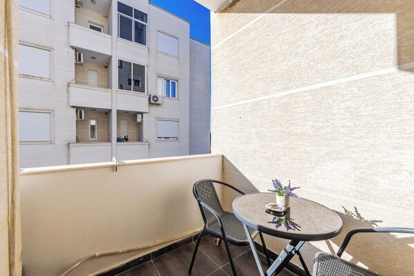 Un balcón con mesa y sillas, con vistas a un edificio con múltiples ventanas y balcones.