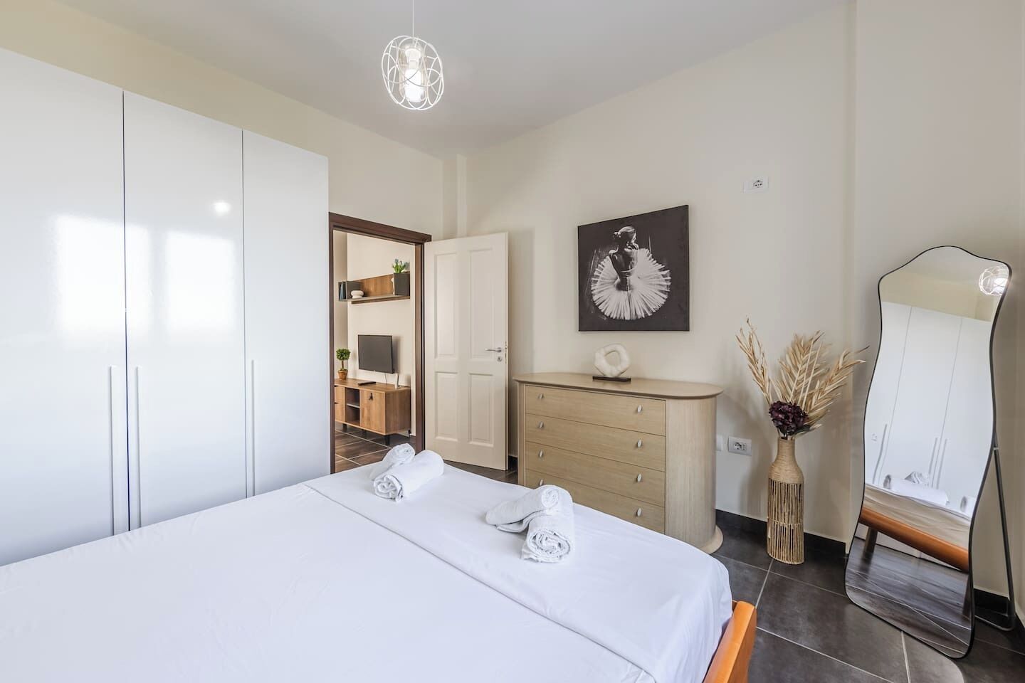 A modern hotel room with a large bed, a wooden dresser, a flat-screen TV, a mirror, and a painting on the wall.