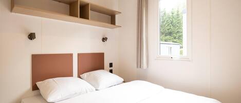 A bedroom with a bed, two bedside tables, a window with curtains, and a wall-mounted shelf.