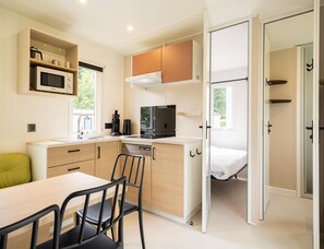 A compact kitchen with a microwave, coffee maker, and a small dining area with a table and chairs. - Cordelia Lodge With Garden & Picnic Area (Ravels)