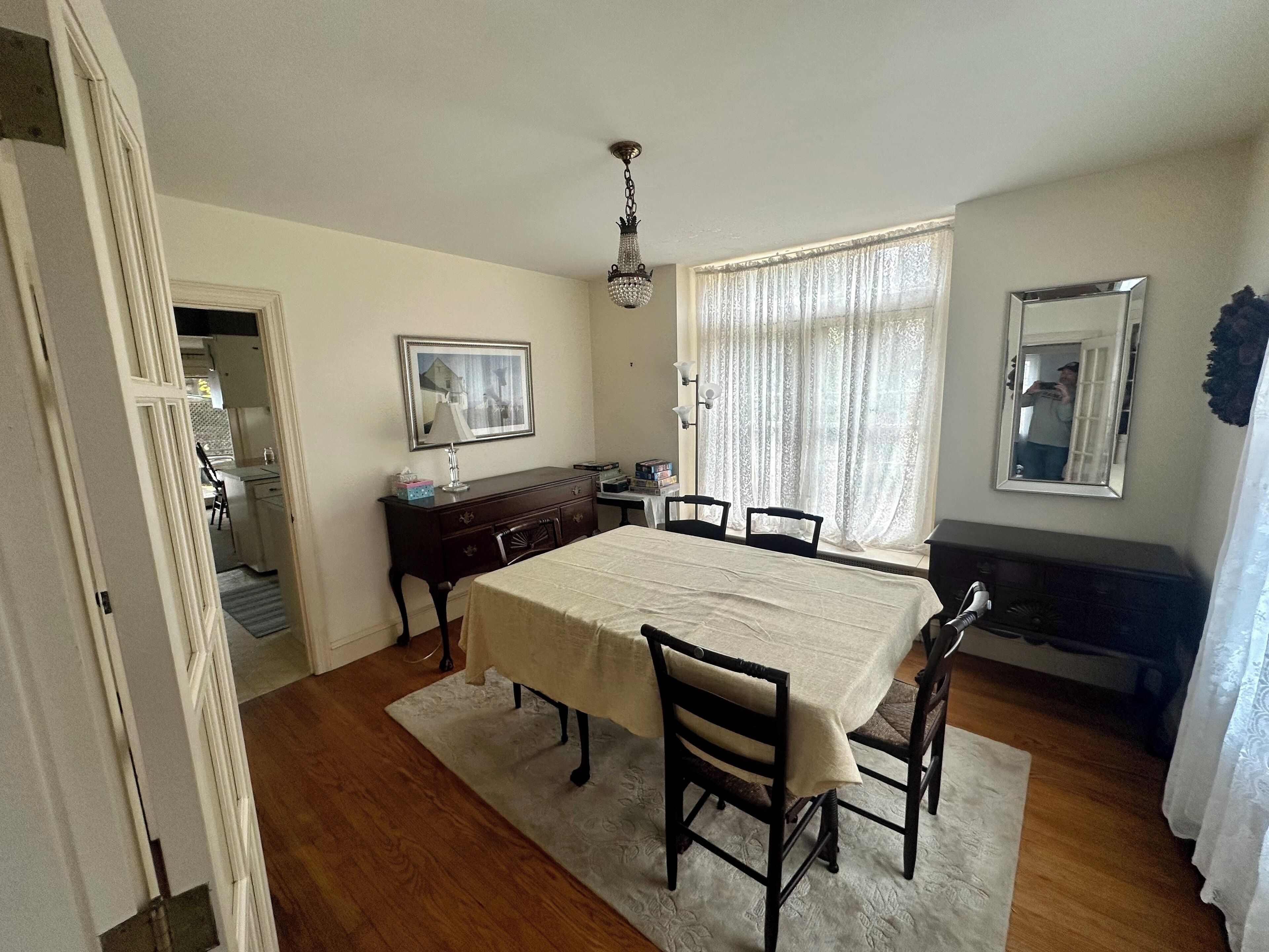Une salle à manger avec une grande table, des chaises, un lustre, une commode et un miroir.