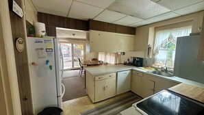 A compact kitchen with a refrigerator, stove, and sink. There is a window with curtains and a door leading to a patio.