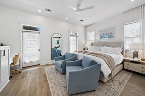 Ein modernes Schlafzimmer mit einem großen Bett, zwei Sesseln, einem Schreibtisch und einem Fenster mit Jalousien.