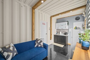 A modern living room with a blue sofa, a wooden ceiling, and a kitchen in the background. - Cozy 1BR Apartment with Private Entrance (Vega Baja)
