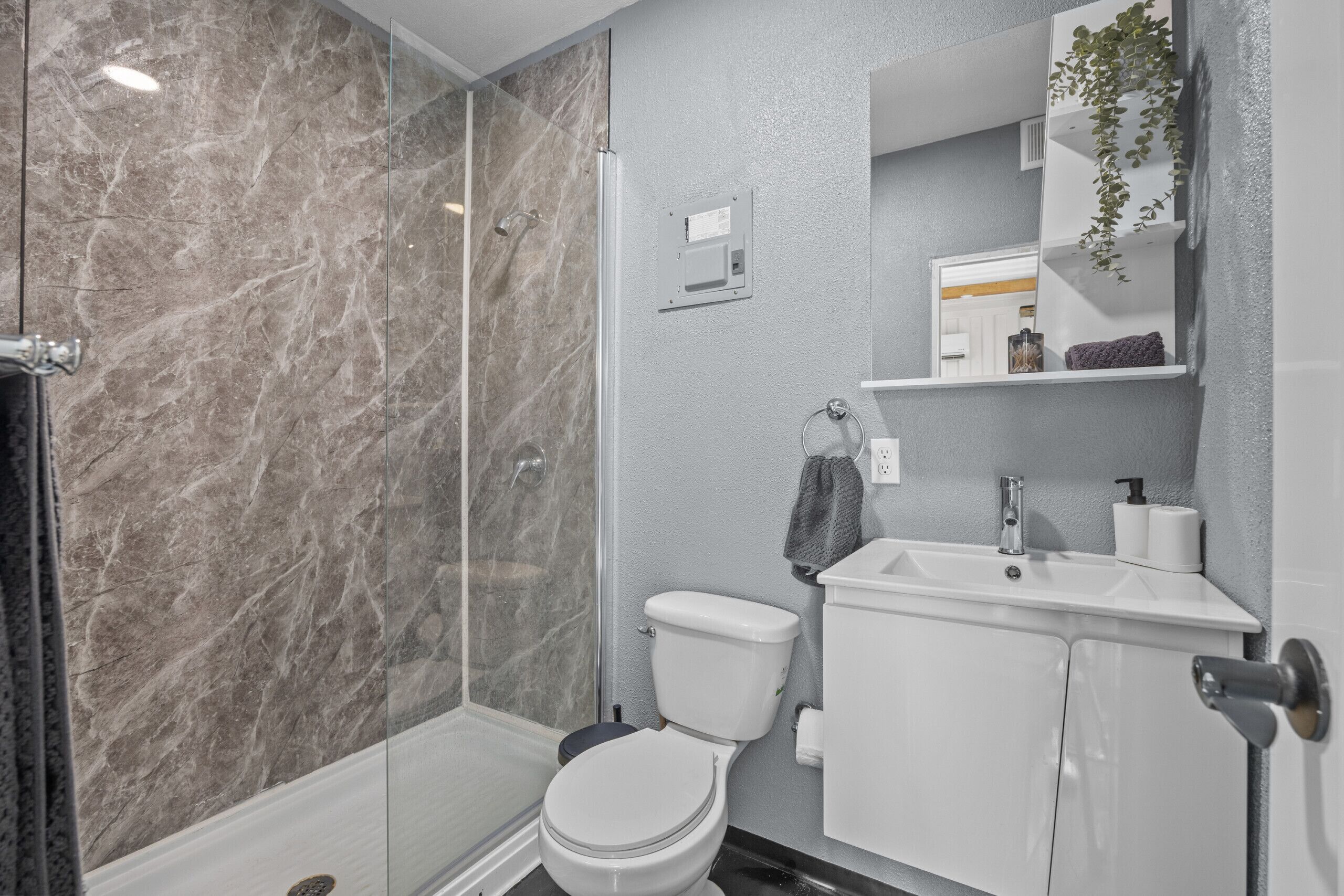 Ein modernes Badezimmer mit Duschkabine aus Glas, einer weißen Toilette und einem Waschbecken mit Spiegel darüber.