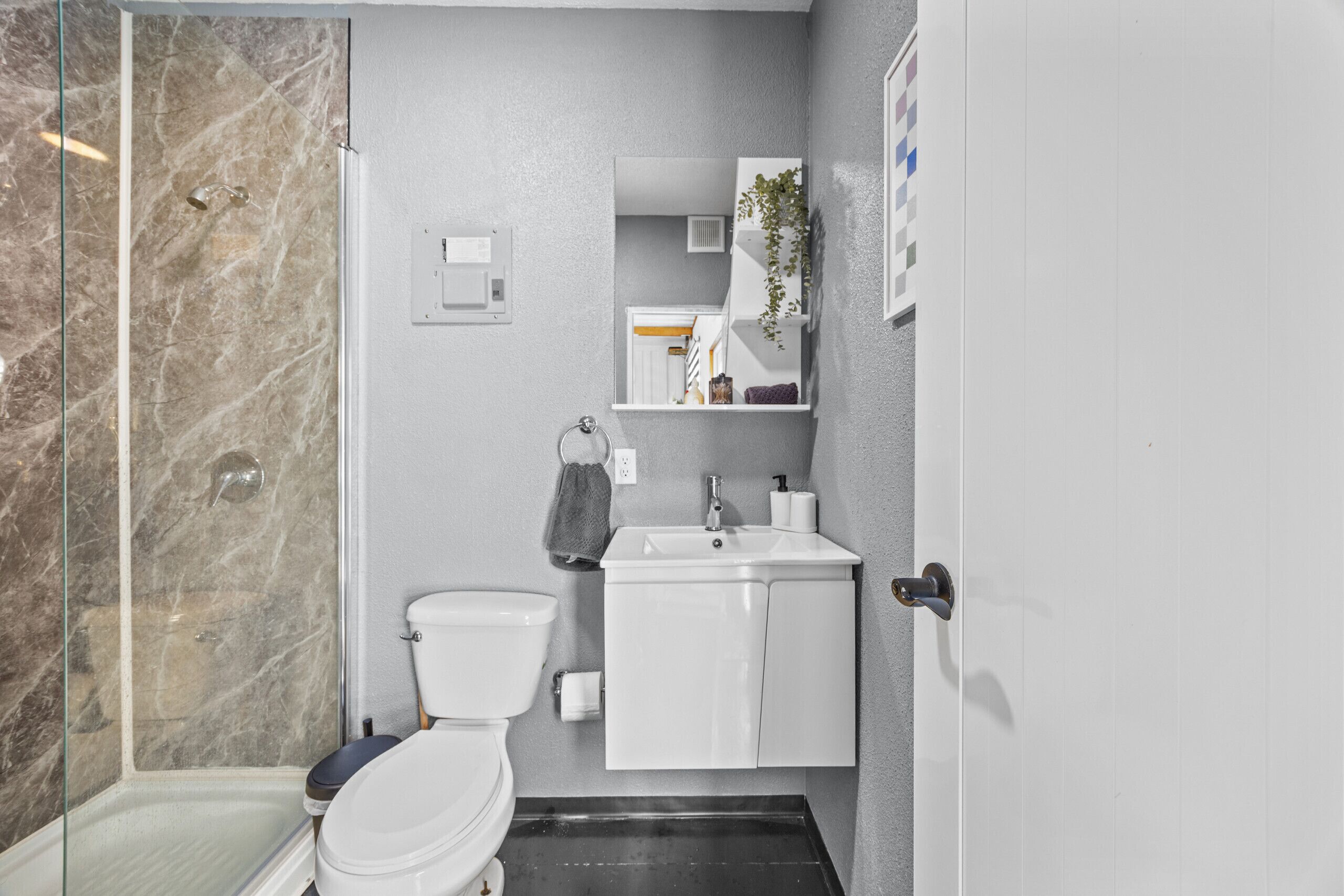 Een badkamer met een glazen douchecabine, toilet, wastafel met spiegel erboven en een handdoek aan de muur.