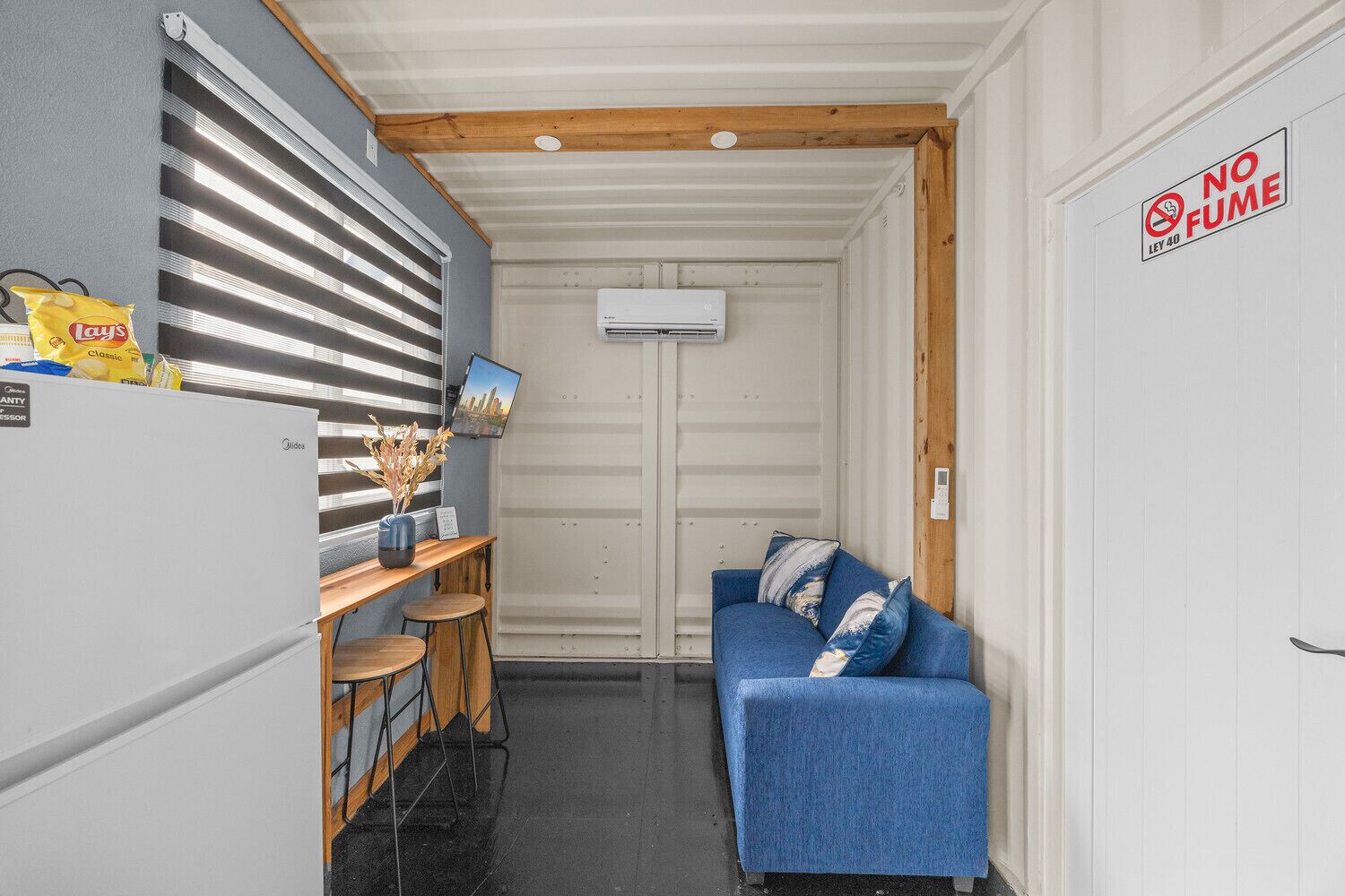 Ein kompaktes Zimmer mit einer Küchenzeile, einem blauen Sofa und einem Schild mit der Aufschrift 'No Fume'.