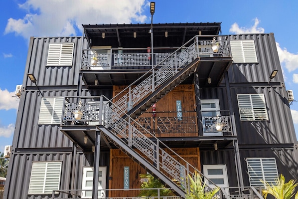 A multi-story building with a staircase connecting the floors, metal railings, and windows with white shutters.