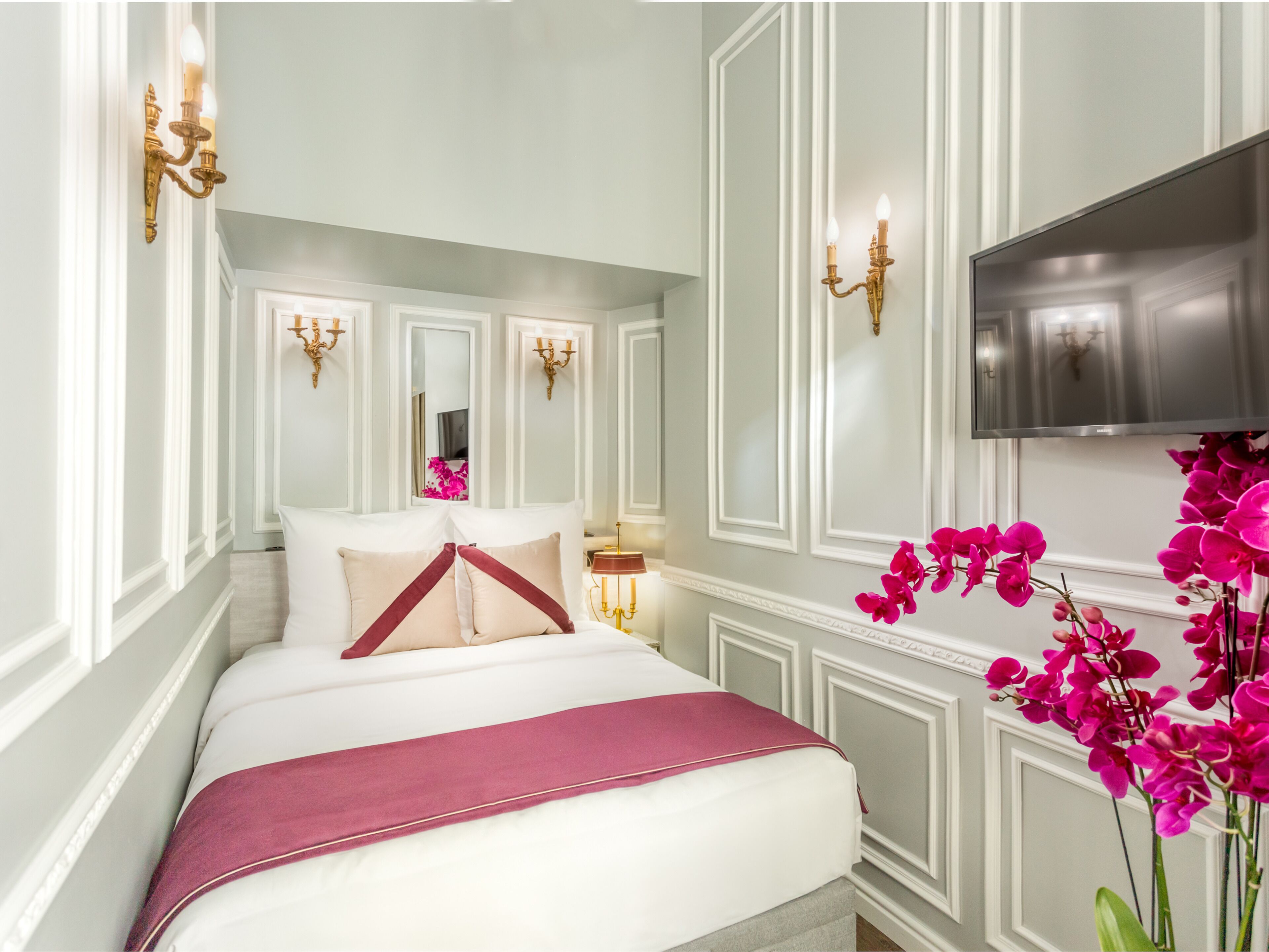 A bedroom with a large bed, white walls, and decorative wall sconces.