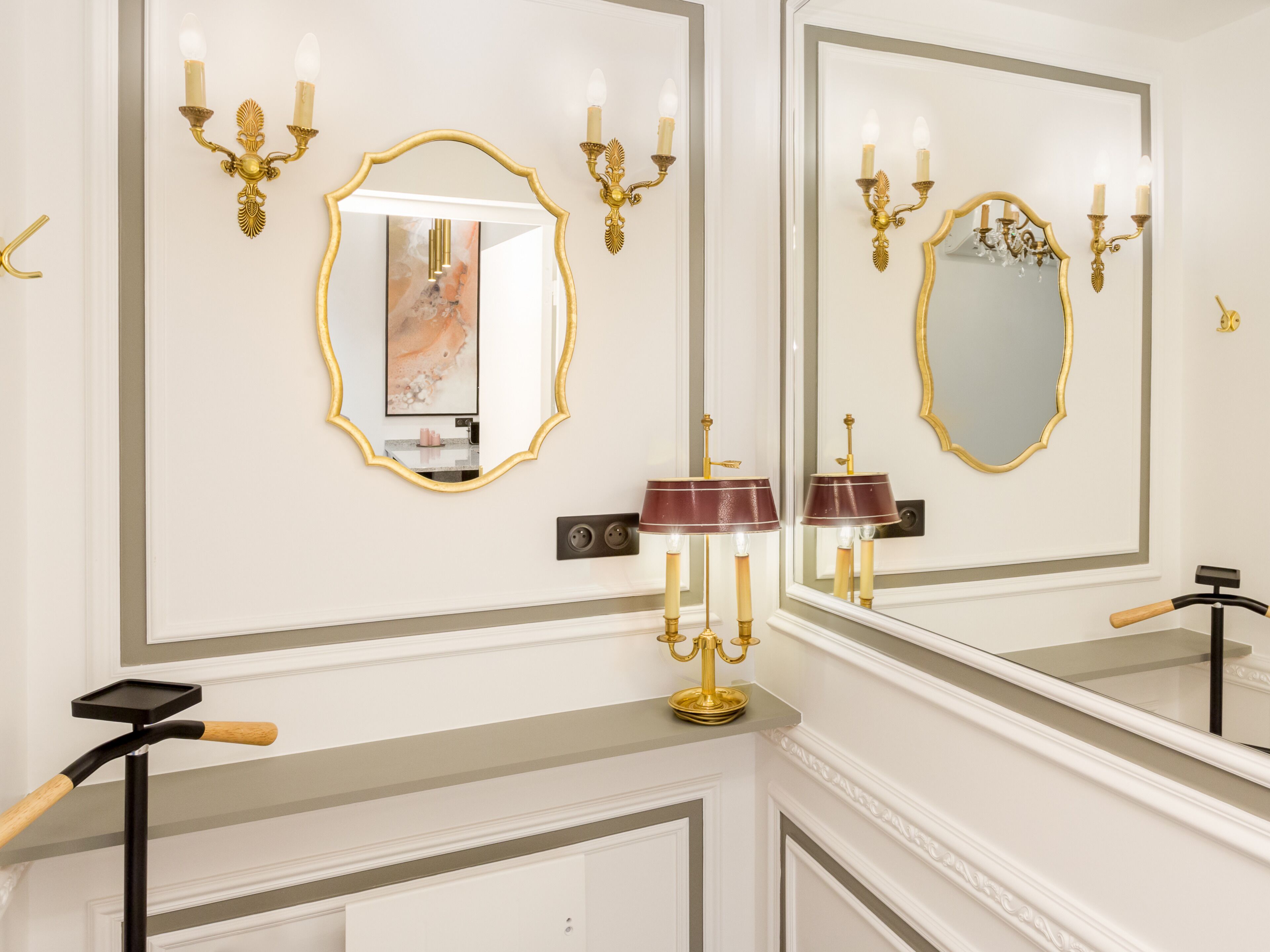 A bathroom with two mirrors, gold sconces, and a marble countertop.