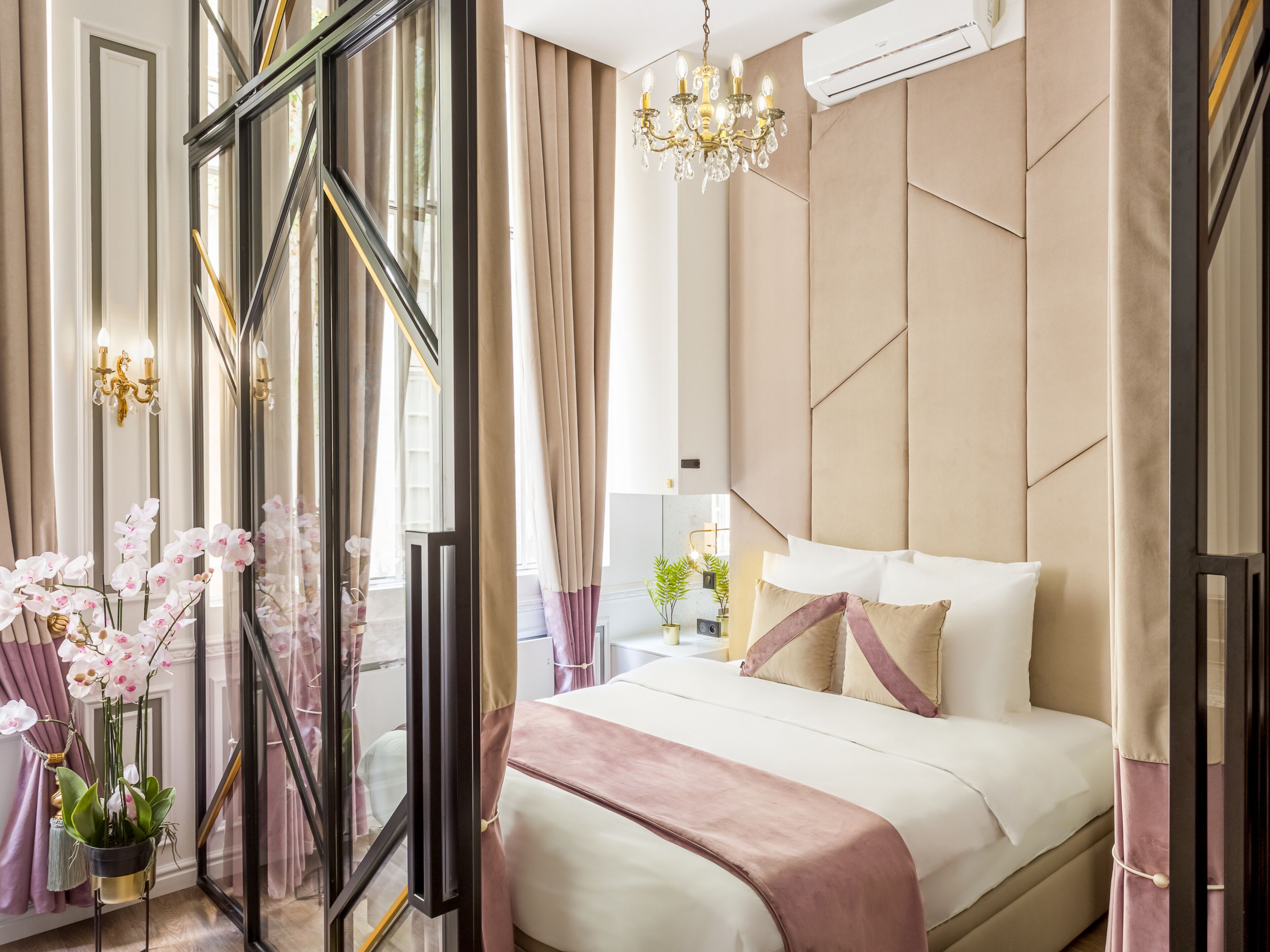 Quarto de hotel moderno com uma cama grande, um candelabro e vista através de uma porta de vidro.
