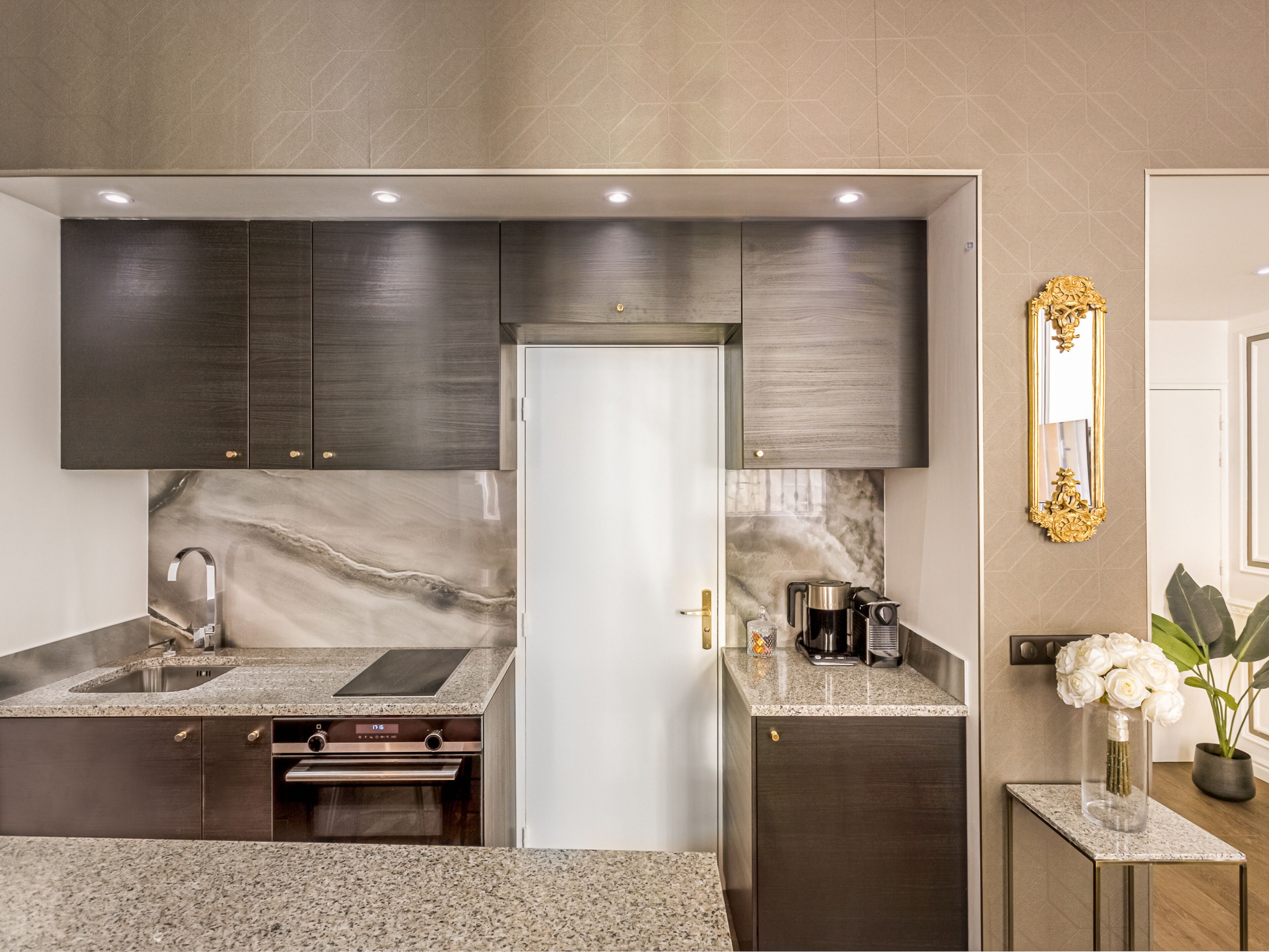 A modern kitchen with dark cabinets, a marble backsplash, and stainless steel appliances.
