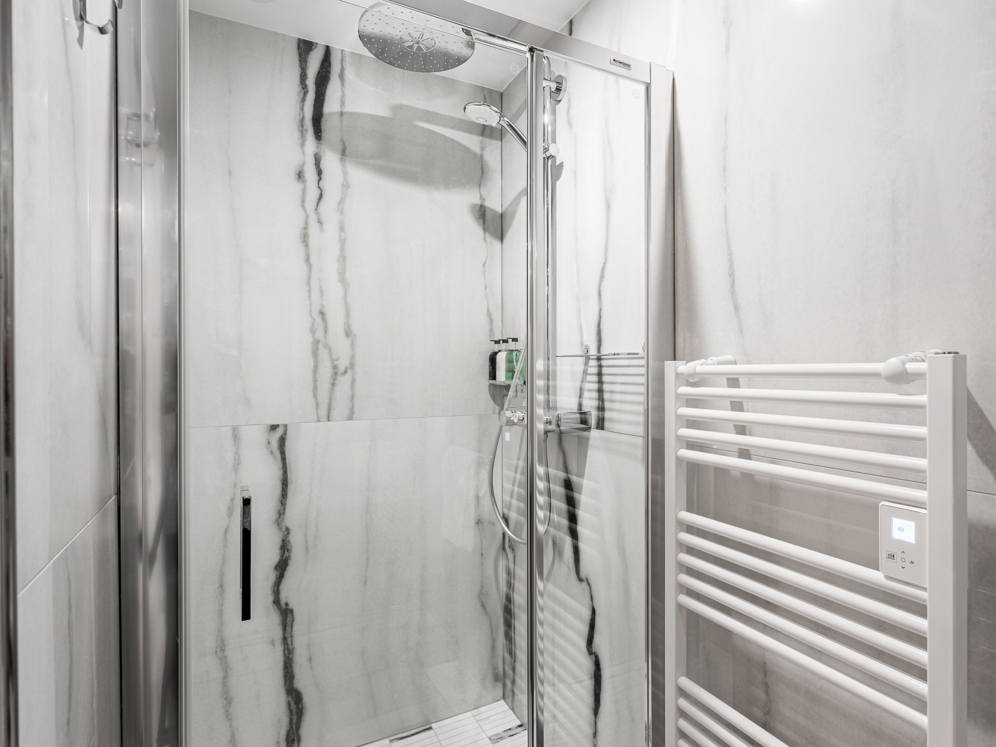 A modern bathroom with a glass-enclosed shower, marble walls, and a white towel rack with a control panel.
