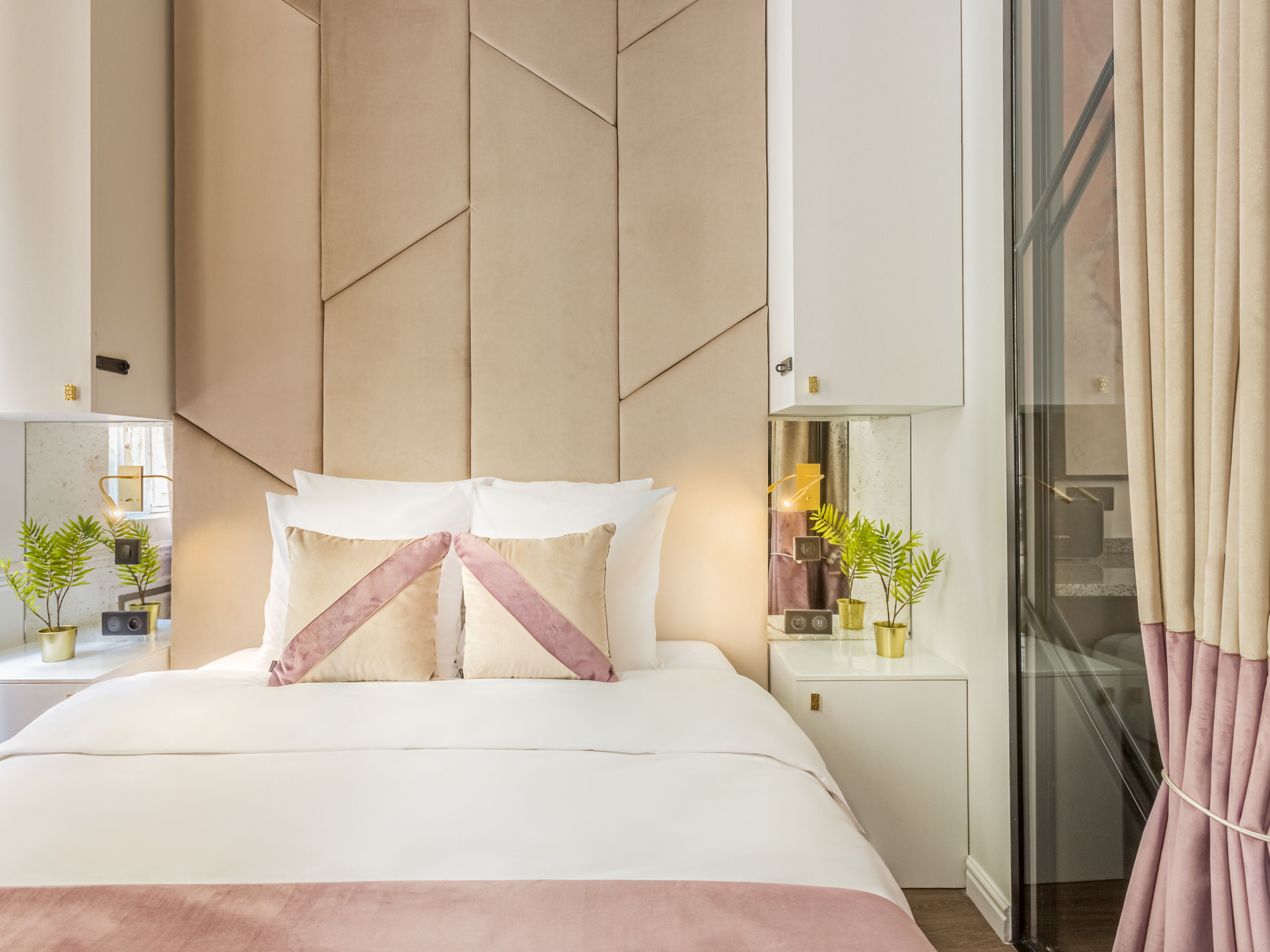 Ein modernes Schlafzimmer mit einem großen Bett, einem Kopfteil mit geometrischen Mustern, Nachttischen mit Lampen und Blick durch eine Glasdoor nach draußen.
