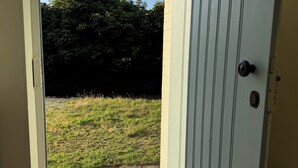 Eine Tür, die zu einer grünen Fläche mit Fußmatte und einer Steinmauer im Hintergrund führt.