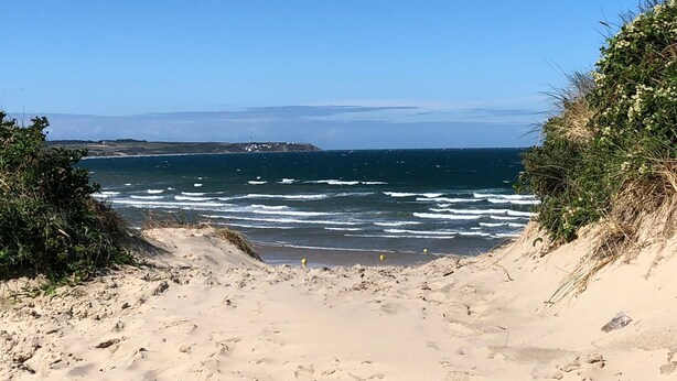 Ein Strand mit freiem Blick auf das Meer und entferntes Land.