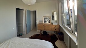 Ein Schlafzimmer mit Bett, Schminktisch, Spiegel und Fenster.