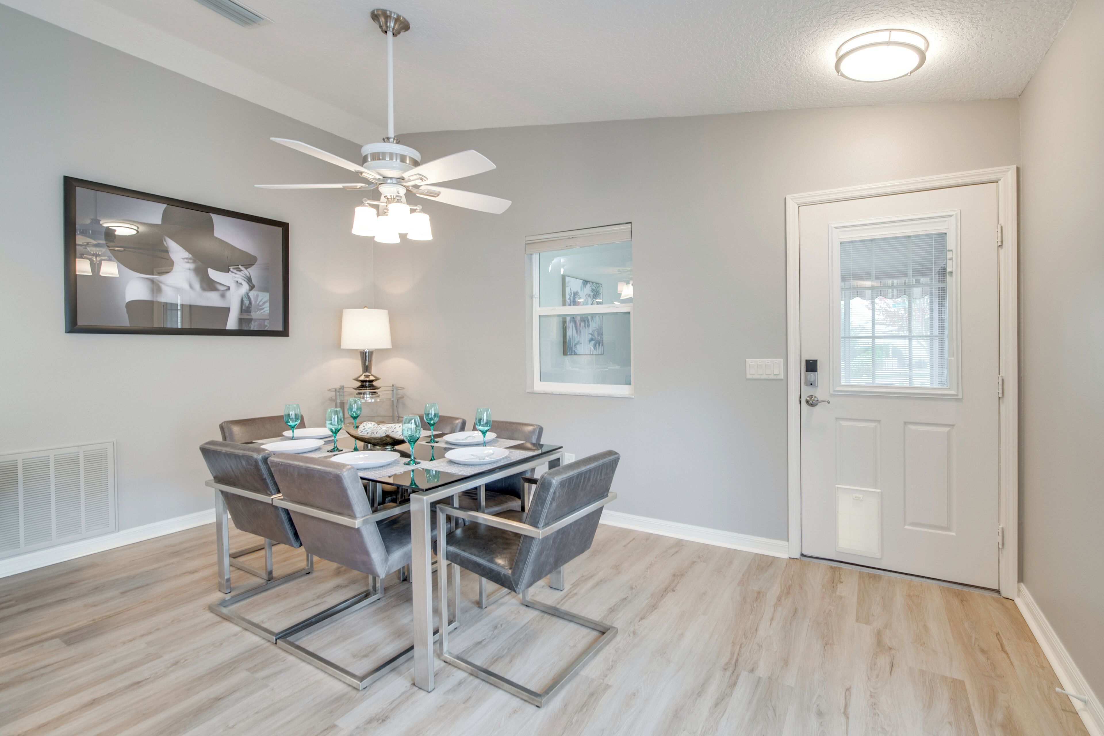 Un coin repas avec une table dressée pour quatre personnes, un ventilateur de plafond et une porte avec une fenêtre.