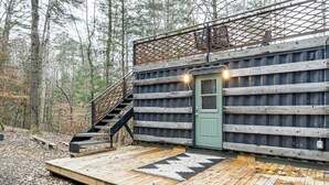 Un chalet rustique doté d’une terrasse en bois, d’une porte verte et d’un escalier menant à un balcon.