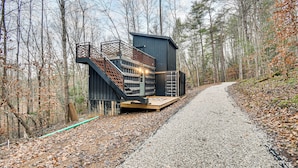 Une cabane dotée d’une terrasse en bois et d’un escalier, entourée d’une forêt.