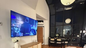 Una sala de estar moderna con un televisor de pantalla plana, muebles de madera y un ventanal amplio.