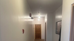 Un pasillo estrecho con alfombra, una puerta de madera al final y un banco con un abrigo colgado.