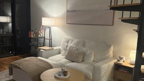Una sala de estar moderna con un sofá, una mesa redonda de centro, una mesita auxiliar con una lámpara y una escalera.