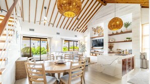 A spacious dining area with a round table and chairs, a kitchen with a large island, and a view of greenery outside.