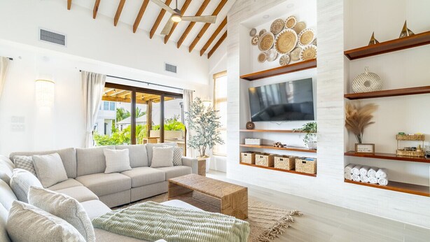 A modern living room with a sectional sofa, a flat-screen TV mounted on the wall, and a wooden ceiling.