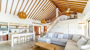 A spacious living area with a large grey sofa, a wooden coffee table, and a kitchen area with a bar.