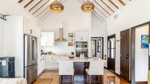Een moderne keuken met witte kasten, een centraal eiland met barkrukken, roestvrijstalen apparatuur en een houten plafond.