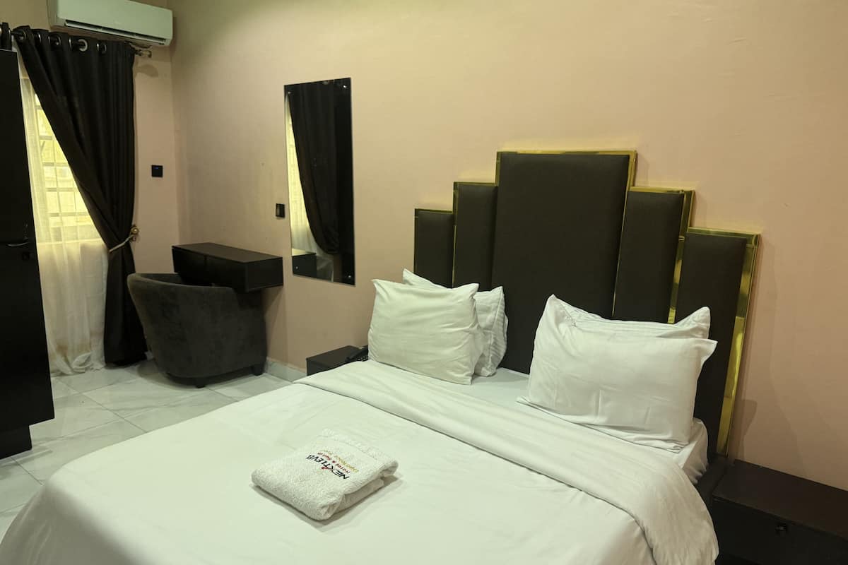 Quarto de hotel com cama, escrivaninha, cadeira e espelho.