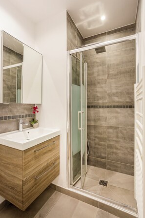 Une salle de bain moderne avec une douche à l’italienne en verre, un meuble-lavabo en bois avec un lavabo blanc et un miroir au-dessus du meuble.