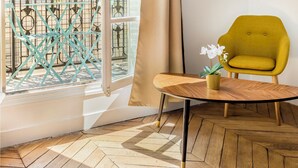 Ein Zimmer mit großem Fenster, einem gelben Sessel, einem kleinen Tisch und einer Topfpflanze.