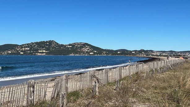 Une vue sur la côte, avec une clôture en bois, une plage et des collines en arrière-plan.