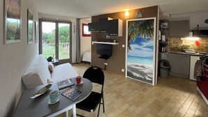 Un espace de vie compact comprenant un coin repas, une kitchenette et une porte-fenêtre coulissante donnant sur un balcon.