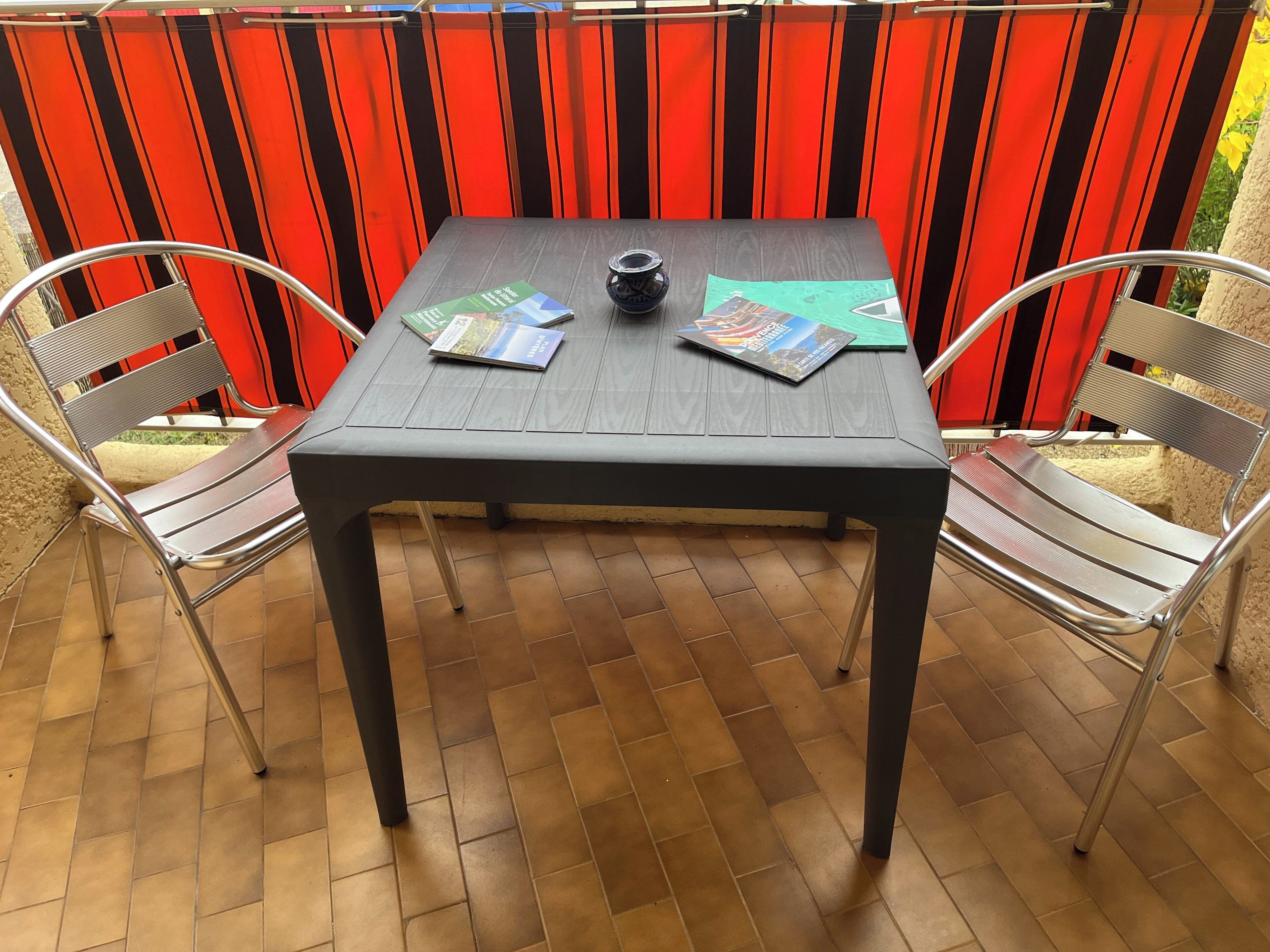 A table with a dark tablecloth, two metal chairs, and a black pot on the table.