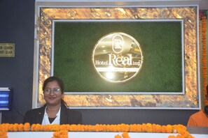 A hotel reception desk with a sign that reads 'Hotel Real in Stay, Celebrate, Repeat.' - HOTEL REAL INN (Muzaffarpur)