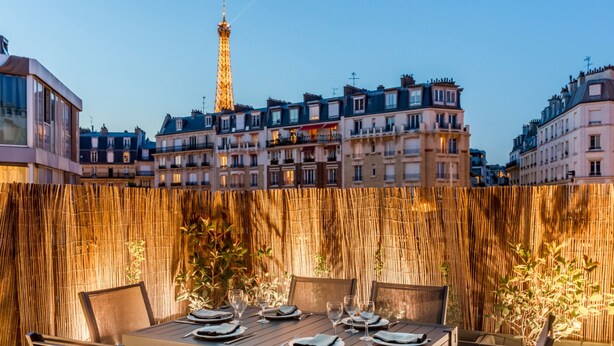 An outdoor dining area with a view of the Eiffel Tower in the background, surrounded by buildings. - Signature Suite Eiffel Tower terrace (Paris)