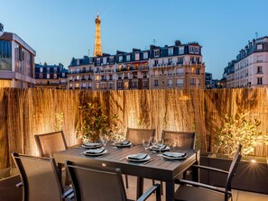 Un área de comedor al aire libre con vista a la Torre Eiffel, rodeada de edificios.