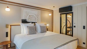 A modern hotel room with a large bed, a small side table, a wall-mounted TV, and a bathroom with a glass door. - Signature Suite Eiffel Tower terrace (Paris)