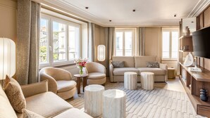 A spacious living room with a large sofa set, a coffee table, and a TV on a wooden stand. - Signature Suite Eiffel Tower terrace (Paris)
