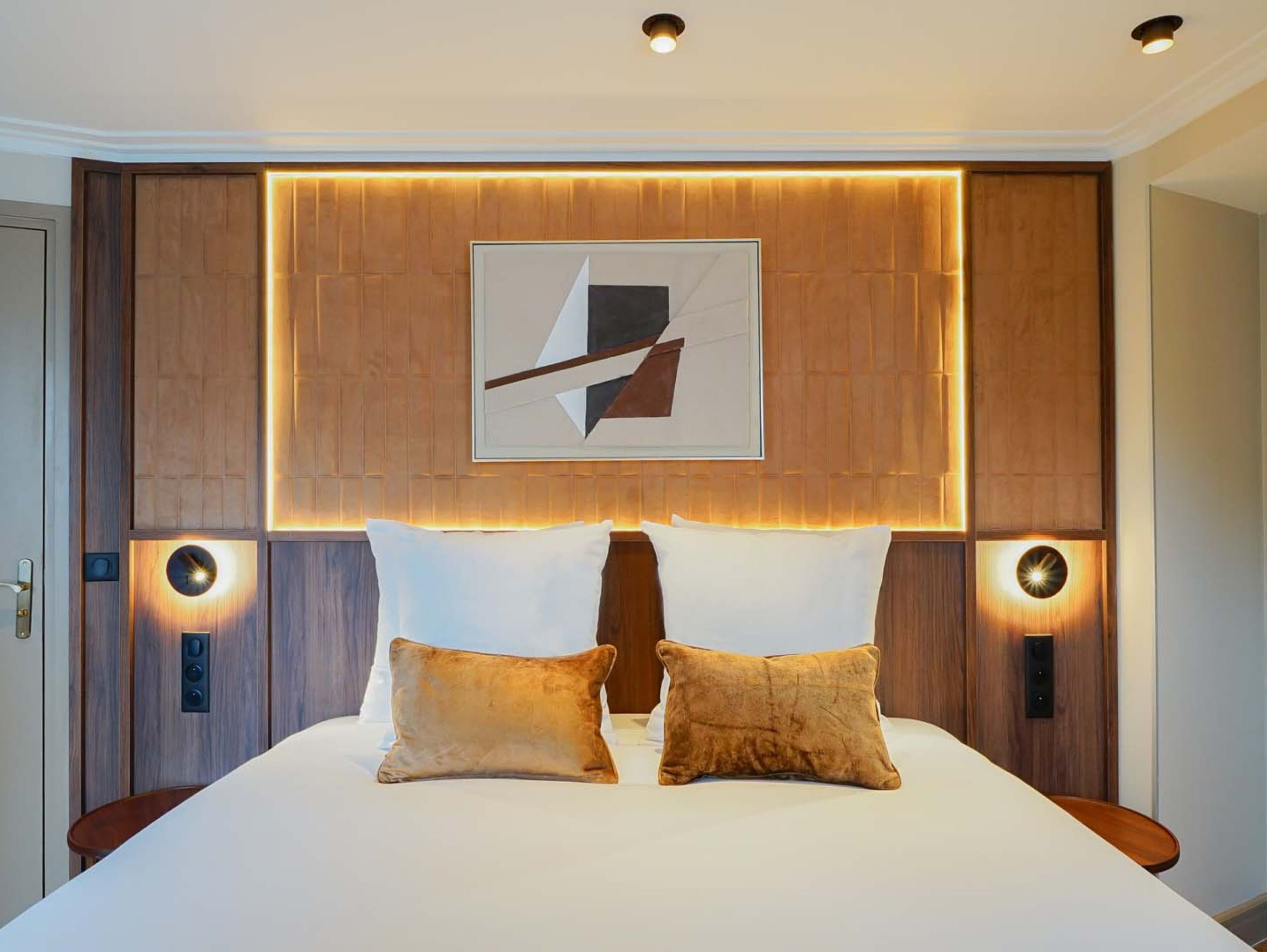 Una habitación de hotel con una cama grande, dos mesitas de noche, una obra de arte en la pared e iluminación empotrada.