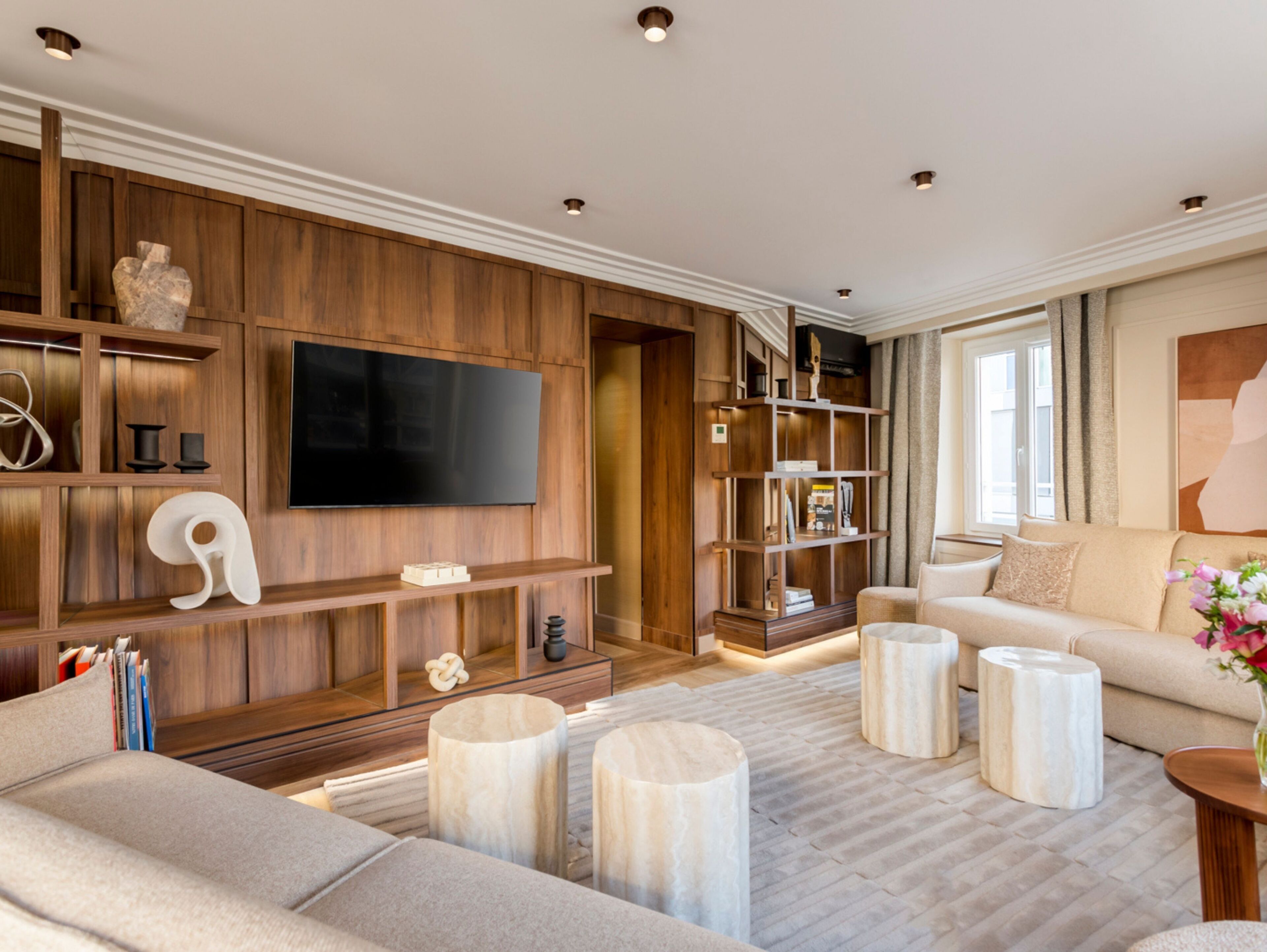 A modern living room with a large flat-screen TV mounted on a wooden wall, a beige sofa, and a coffee table.