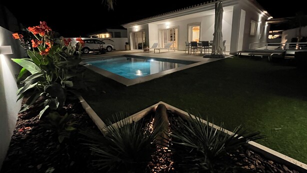 A nighttime view of a residential property with a swimming pool, outdoor seating, and a well-lit patio area. - Casa Alegria (Tunes)
