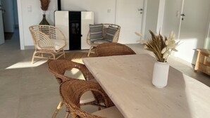 A dining area with a long wooden table, wicker chairs, a hanging light fixture, and a vase with dried plants. - Casa Alegria (Tunes)