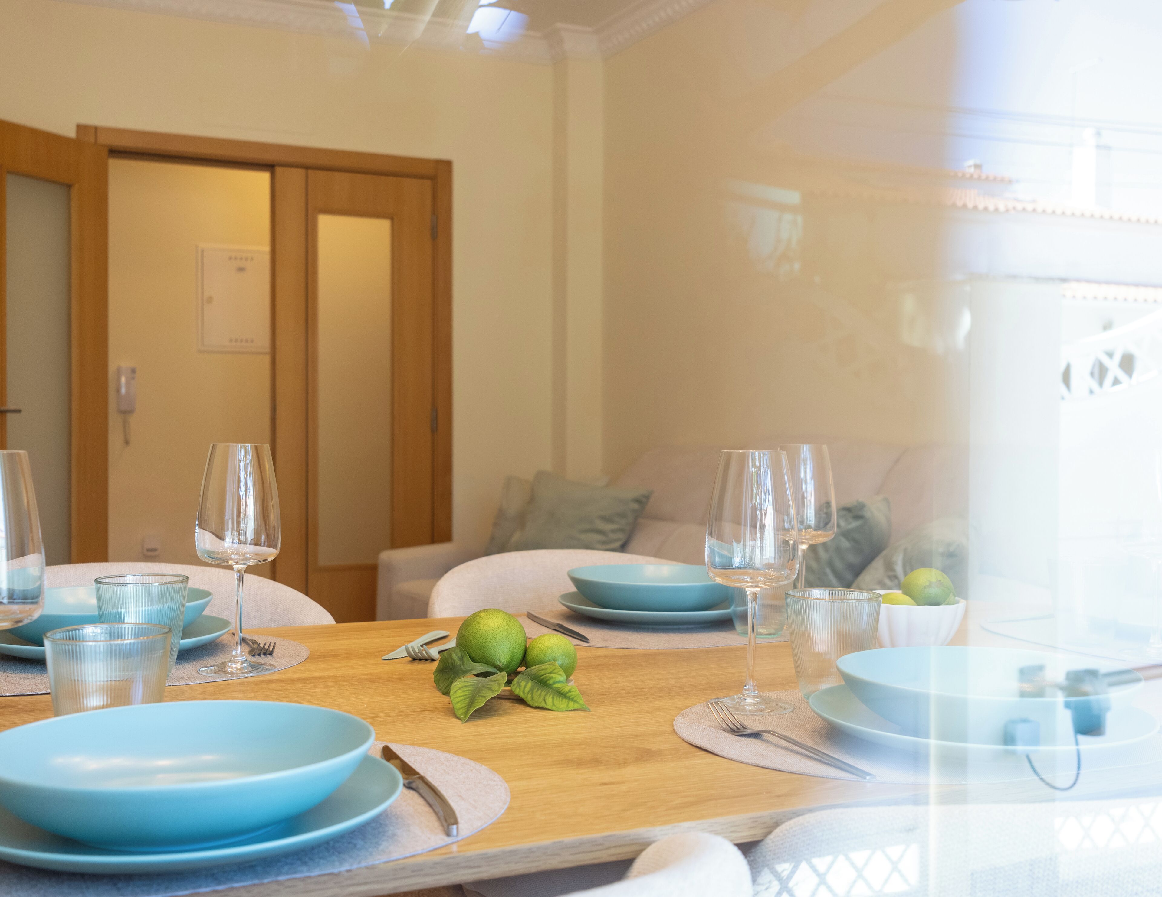 A dining table set with blue plates, wine glasses, and a centerpiece of green fruits.