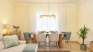 Ein modernes Wohnzimmer mit Essbereich, ausgestattet mit einer Couch, Sesseln, einem Tisch für vier Personen und einem Kronleuchter.