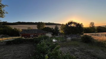 Un paysage rural avec une cabane en bois, de vastes champs et un coucher de soleil en arrière-plan.